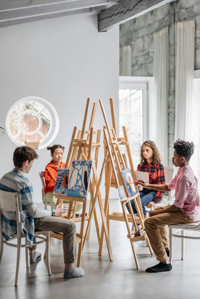 A group of children in a bright room actively participating in an art class, painting on easels.